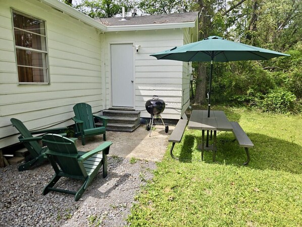 A small house with a patio area featuring outdoor furniture, a grill, and a table with an umbrella. - Stark Social House | Sleeps 6 | Game Day (Starkville)