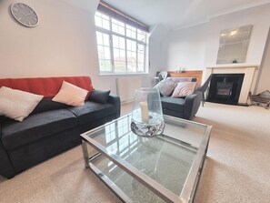 A living room with two dark sofas, a glass coffee table, a fireplace, and a large window.