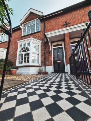 A two-story brick house with a black and white checkered driveway leading to a black door marked with the number 38.