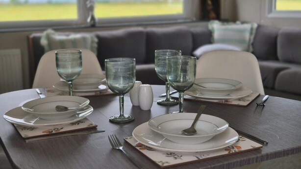 Una mesa de comedor dispuesta con platos, vasos y cubiertos, con vistas al exterior a través de amplias ventanas.