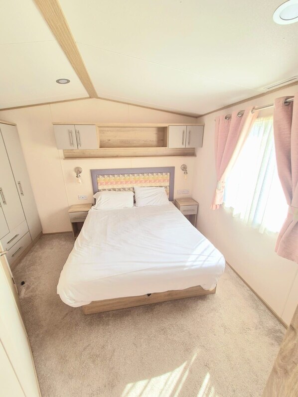 A bedroom with a bed, two bedside tables, a wardrobe, and a window with curtains.