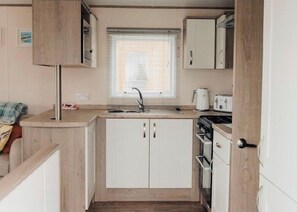 A compact kitchenette with a sink, stove, and white cabinets. - Luxury Seasalter Caravan (Whitstable)
