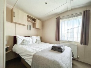 A bedroom with a bed, a radiator, a window with curtains, and built-in shelving.