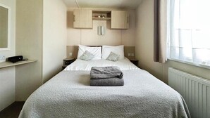 Et hotelværelse med seng, et natbord, en indbygget hylde, et vindue med gardiner og en termostat på væggen.