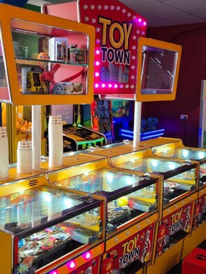 Una fila de máquinas de salón con letrero 'TOY TOWN', mostrando diversos juegos y premios visibles a través del cristal.
