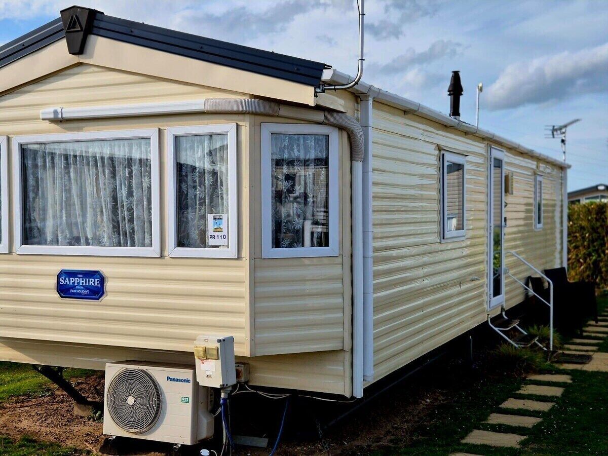 A mobile home with a 'Sapphire' sign, a window with a curtain, and a visible air conditioning unit.