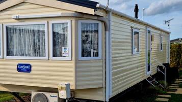 A mobile home with a 'Sapphire' sign, a window with a curtain, and a visible air conditioning unit.