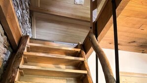 Een houten trap met een rustiek ontwerp, met een stenen muur aan één kant en een houten leuning aan de andere kant.