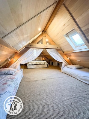 Ein gemütliches Schlafzimmer im Dachgeschoss mit schrägen Wänden, einem Bett mit Baldachin und einem Oberlicht.