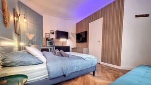Ein modernes Schlafzimmer mit Bett, Sitzgelegenheit, Fernseher und einer Küchenzeile.