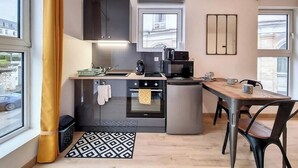 Een kleine keuken met moderne apparaten, een eethoek met een houten tafel, en uitzicht door een raam.