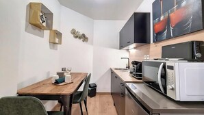 Cocina compacta con microondas, cafetera y comedor con mesa y sillas.
