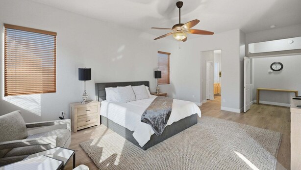 Una camera da letto con un letto, comodini, una ventola a soffitto e vista sull'area soggiorno comunicante.