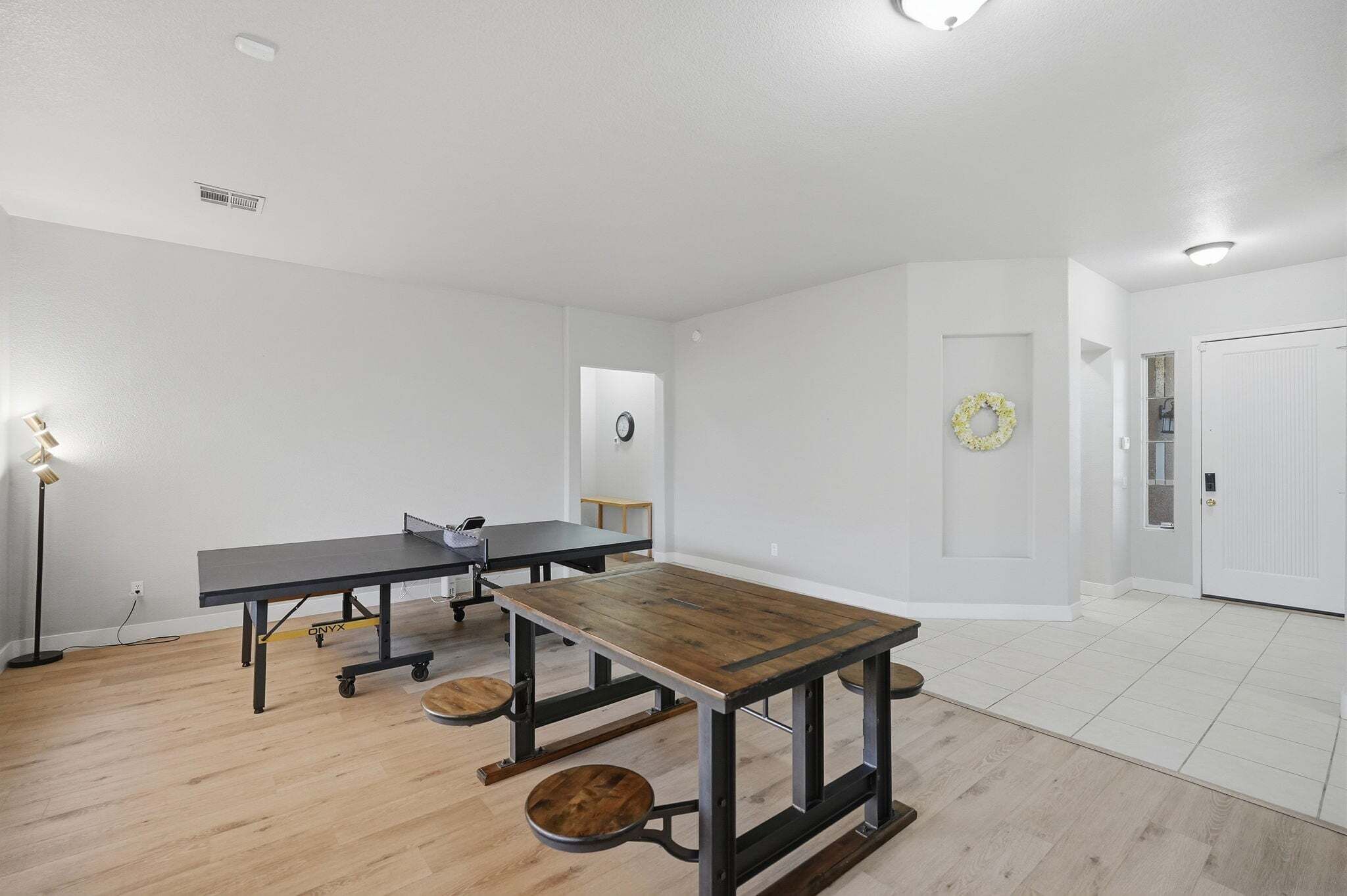 Una habitación amplia con una gran mesa de madera, una mesa de metal negro y una lámpara de pie.
