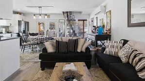 A modern living room with a black sofa, a coffee table, and a dining area with chairs and a table. - Lakefront w/ Private Dock, 2 Slips, Swim Mat, Firepit, & Covered Patio 44mm (Roach)