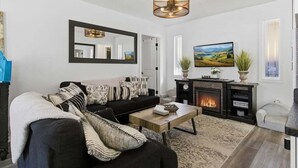 A living room with a black sofa, a wooden coffee table, a fireplace, and a large mirror on the wall. - Lakefront w/ Private Dock, 2 Slips, Swim Mat, Firepit, & Covered Patio 44mm (Roach)