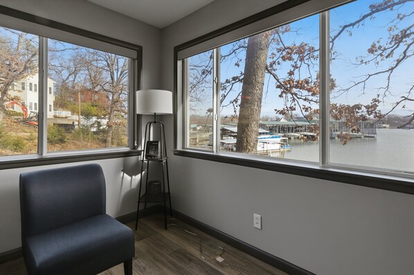 A room with a large window, a chair, and a floor lamp. - Charming & Cozy Waterfront Cabin at 21mm Near Shorty Pants (Osage Beach)