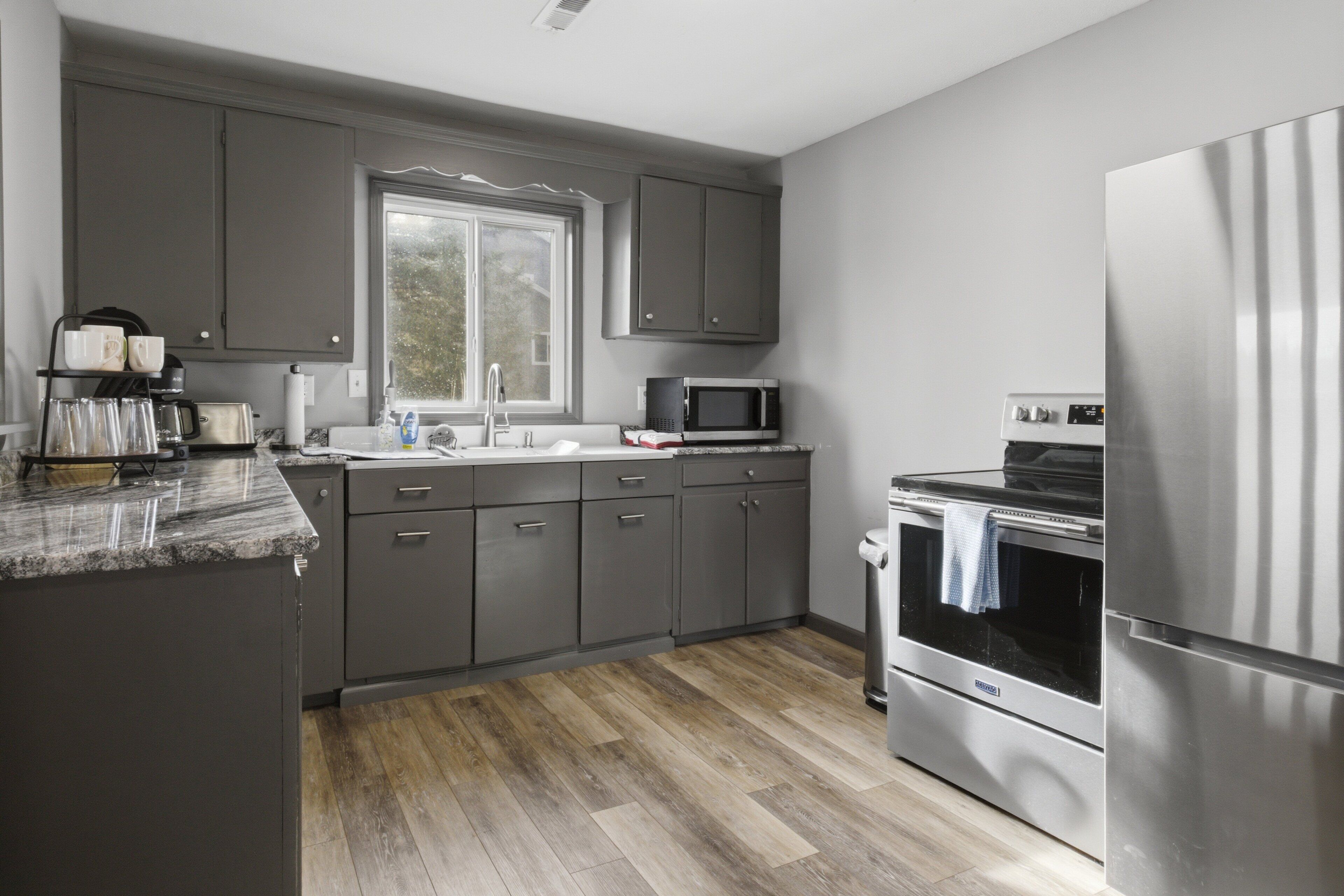 A modern kitchen with grey cabinets, a stainless steel refrigerator, a microwave, and a built-in oven.