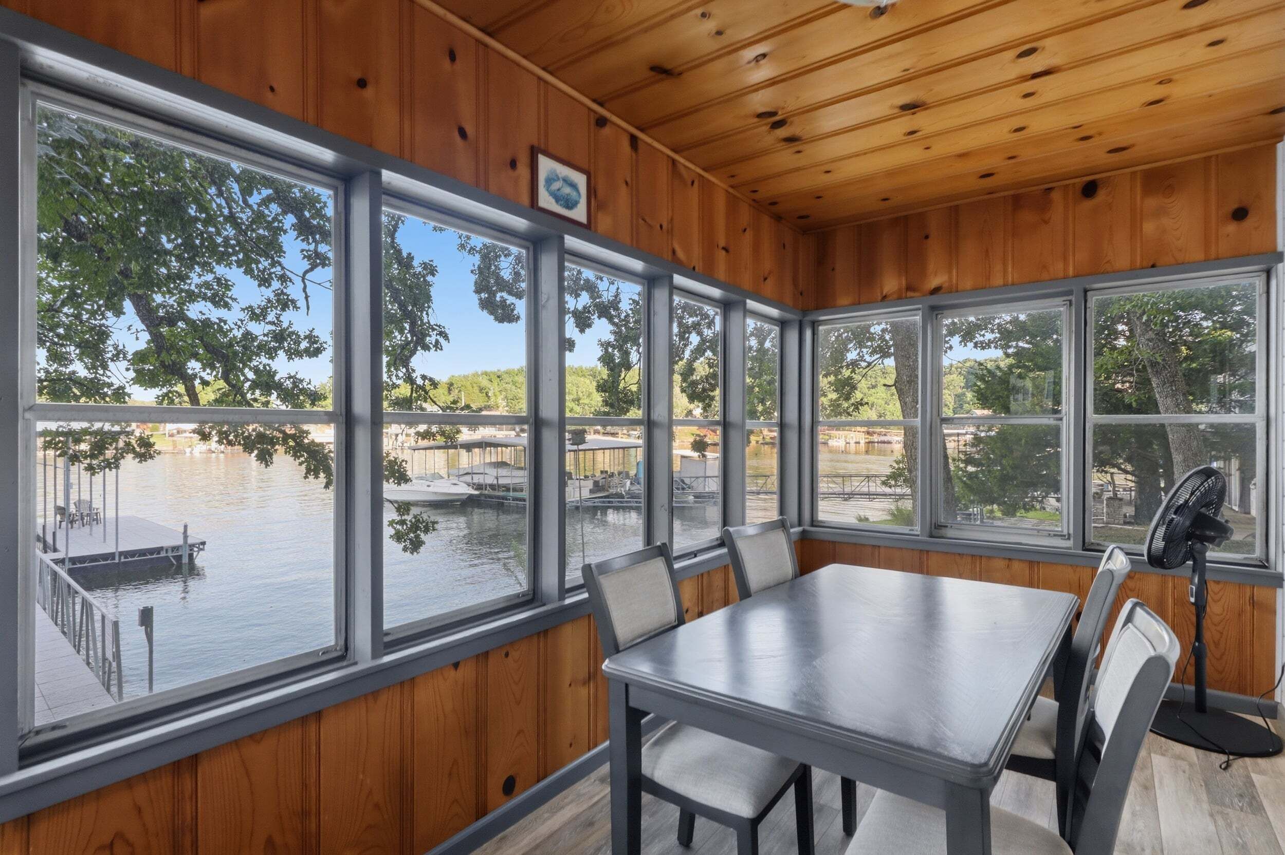 A wooden-paneled room with a large table and chairs, large windows with a view of a dock and water.