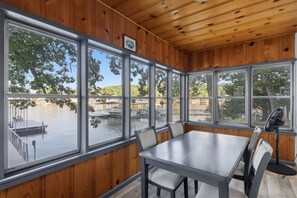 Habitación con paneles de madera, una mesa grande y sillas, y ventanas amplias con vista a un muelle y al agua.