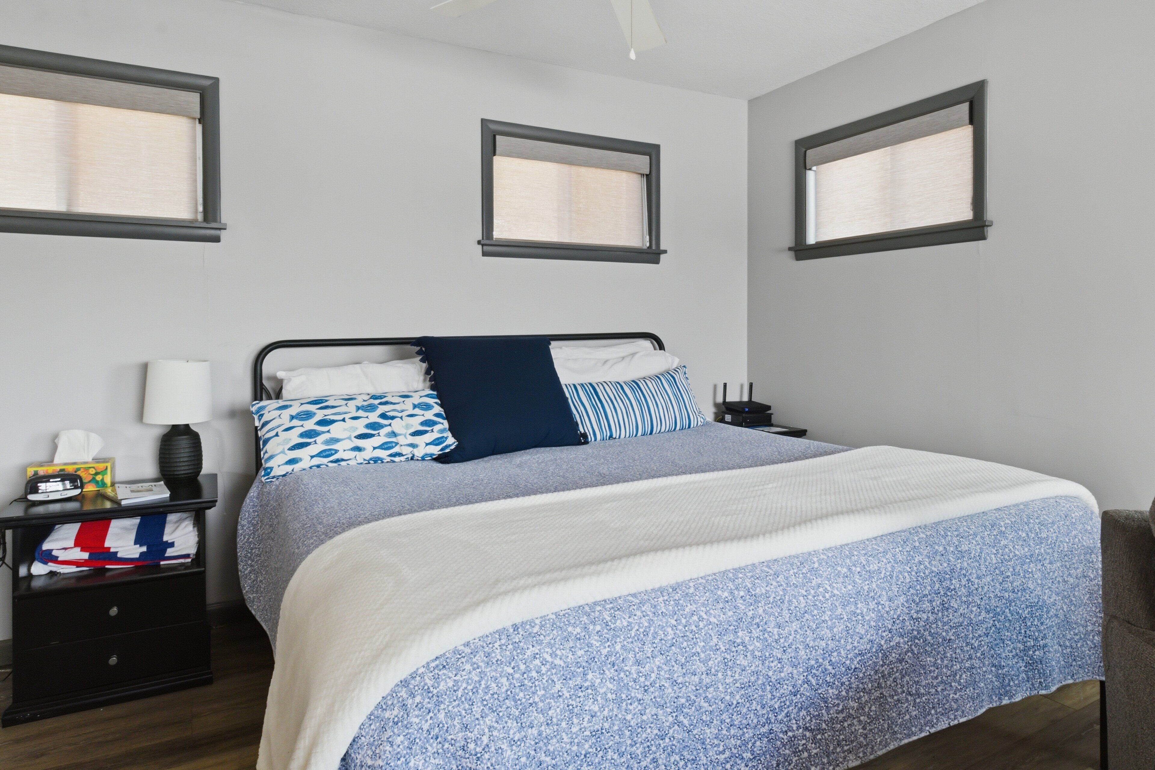 A bedroom with a bed, nightstands, and three windows.