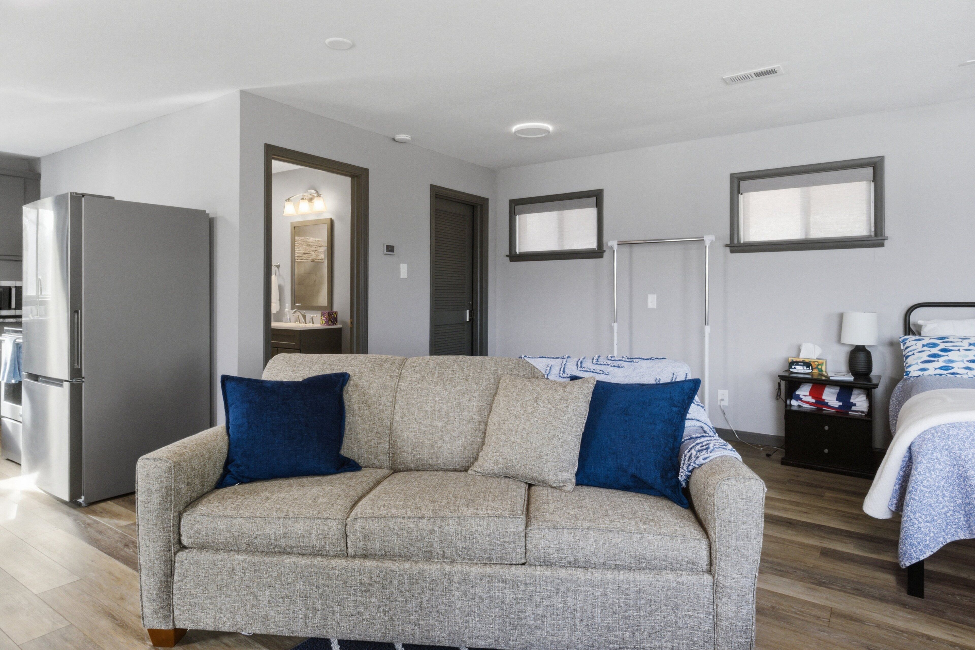 Una sala moderna con sofá, cama, mesita y refrigerador.