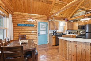 A log cabin interior with a dining area, kitchen, and a blue door. - Lakefront Log Cabin With Private Dock, Two Decks & Cozy Comfort at 35mm in Sunrise Beach (Sunrise Beach)