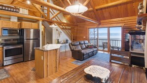 A log cabin interior with a kitchen, dining area, and a seating area with a view of the outdoors. - Lakefront Log Cabin With Private Dock, Two Decks & Cozy Comfort at 35mm in Sunrise Beach (Sunrise Beach)