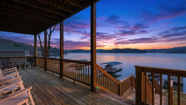 A wooden deck with chairs, overlooking a calm lake at sunset. - Lakefront Log Cabin With Private Dock, Two Decks & Cozy Comfort at 35mm in Sunrise Beach (Sunrise Beach)