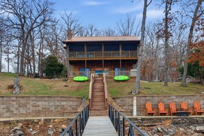 A two-story lodge with a wooden exterior, a stone retaining wall, and a wooden staircase leading to the entrance. - Lakefront Log Cabin With Private Dock, Two Decks & Cozy Comfort at 35mm in Sunrise Beach (Sunrise Beach)