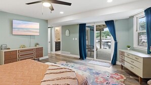 A bedroom with a bed, dresser, ceiling fan, and a view through a sliding glass door. - Spacious Lakefront Home w/ Private Dock, Decks, Game Room & Firepits at the 12mm (Sunrise Beach)