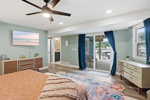 Ein Schlafzimmer mit Bett, Kommode, Deckenventilator und Blick durch eine Schiebetür.