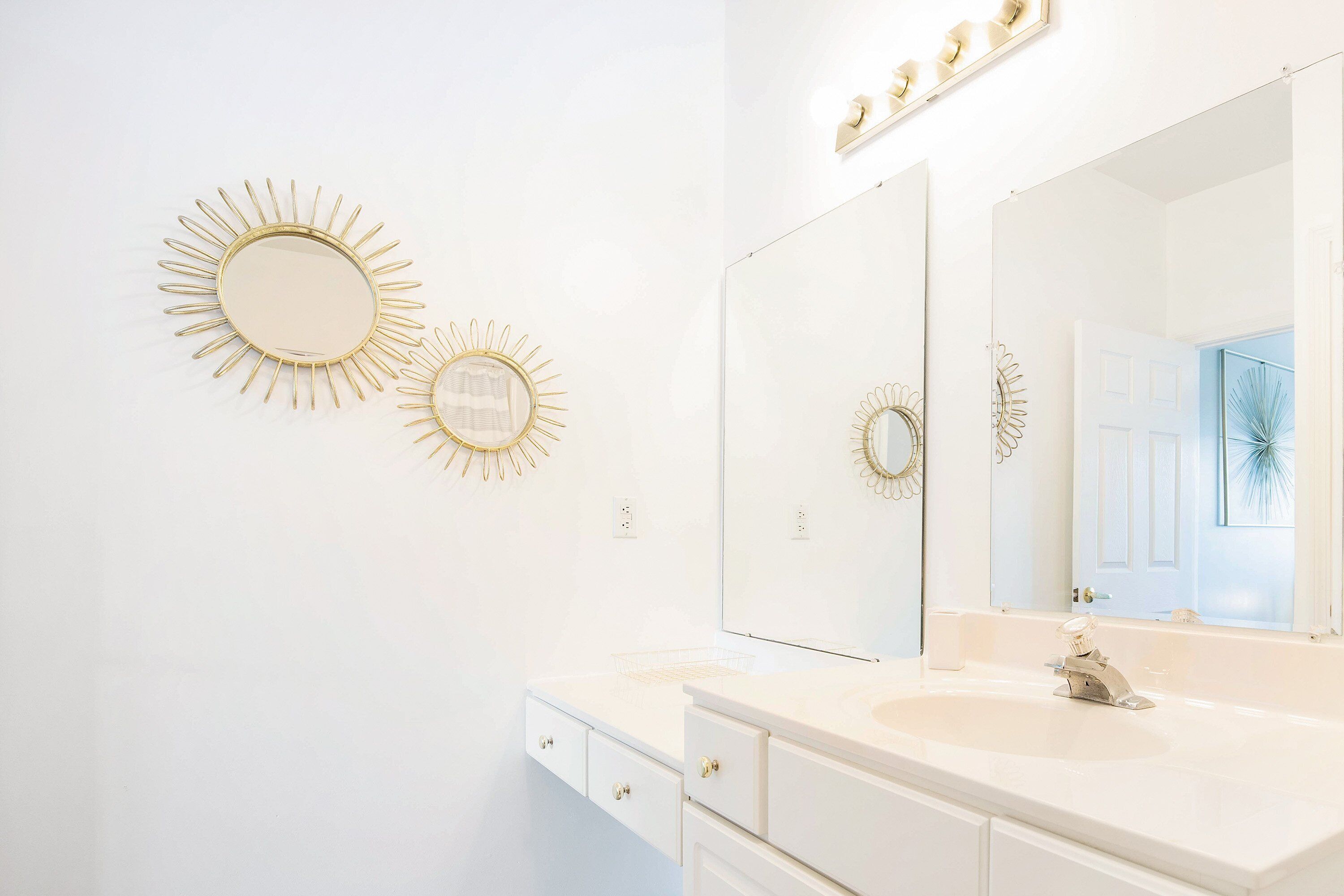 Un baño con un tocador blanco, un espejo grande y dos espejos con forma de sol.