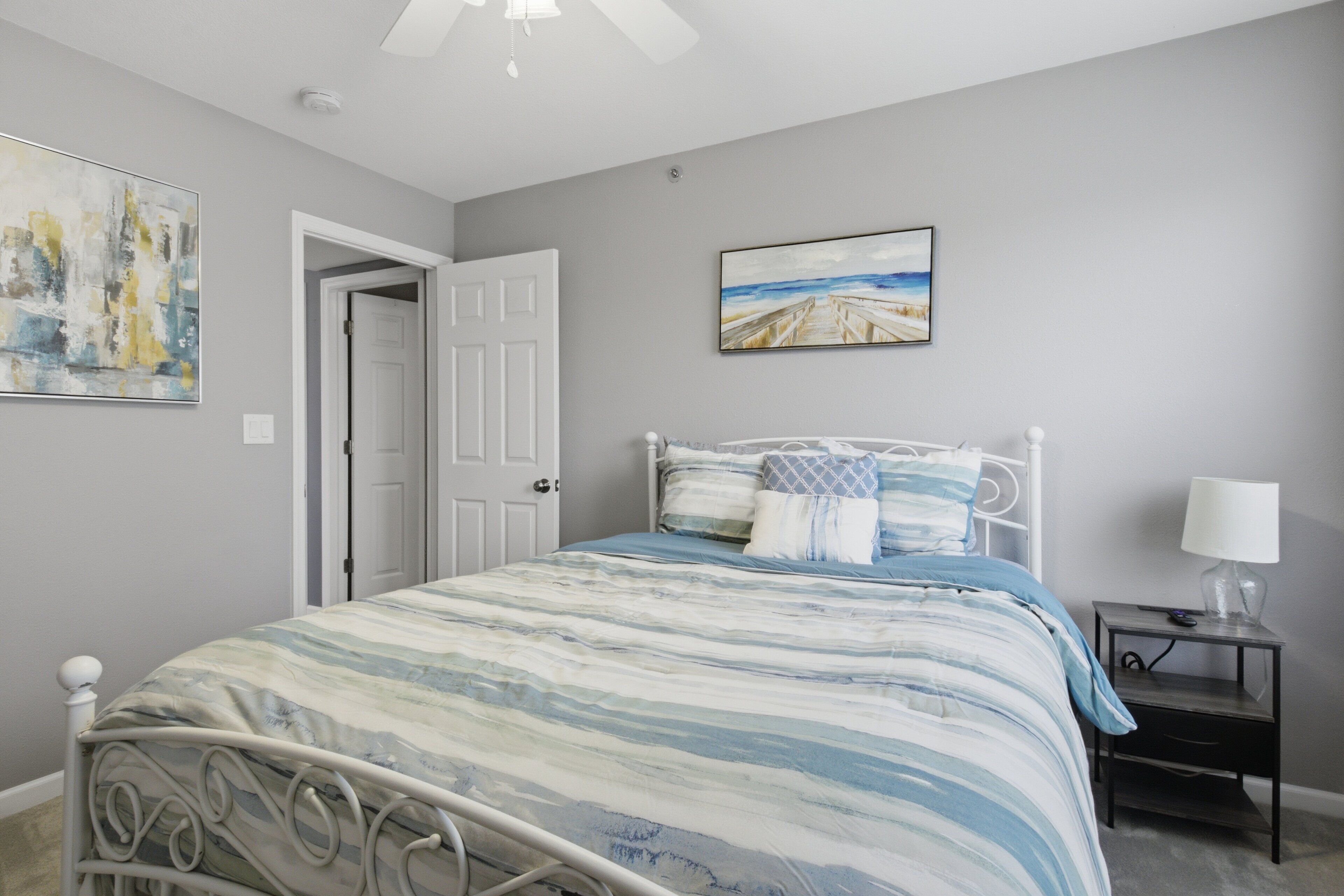 A bedroom with a bed, a nightstand, a door, and a painting on the wall.