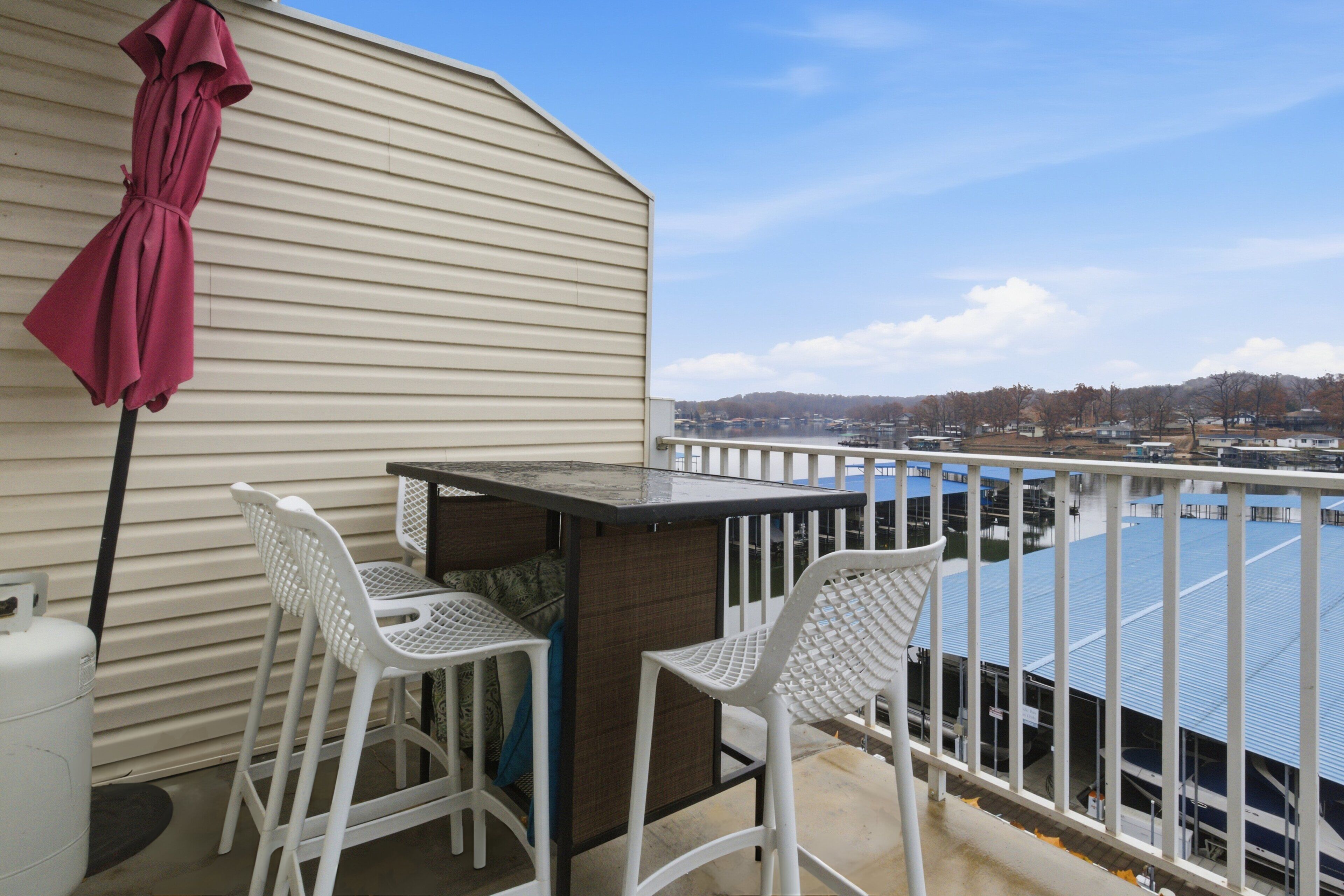 A balcony with two white chairs, a table, and a red umbrella.