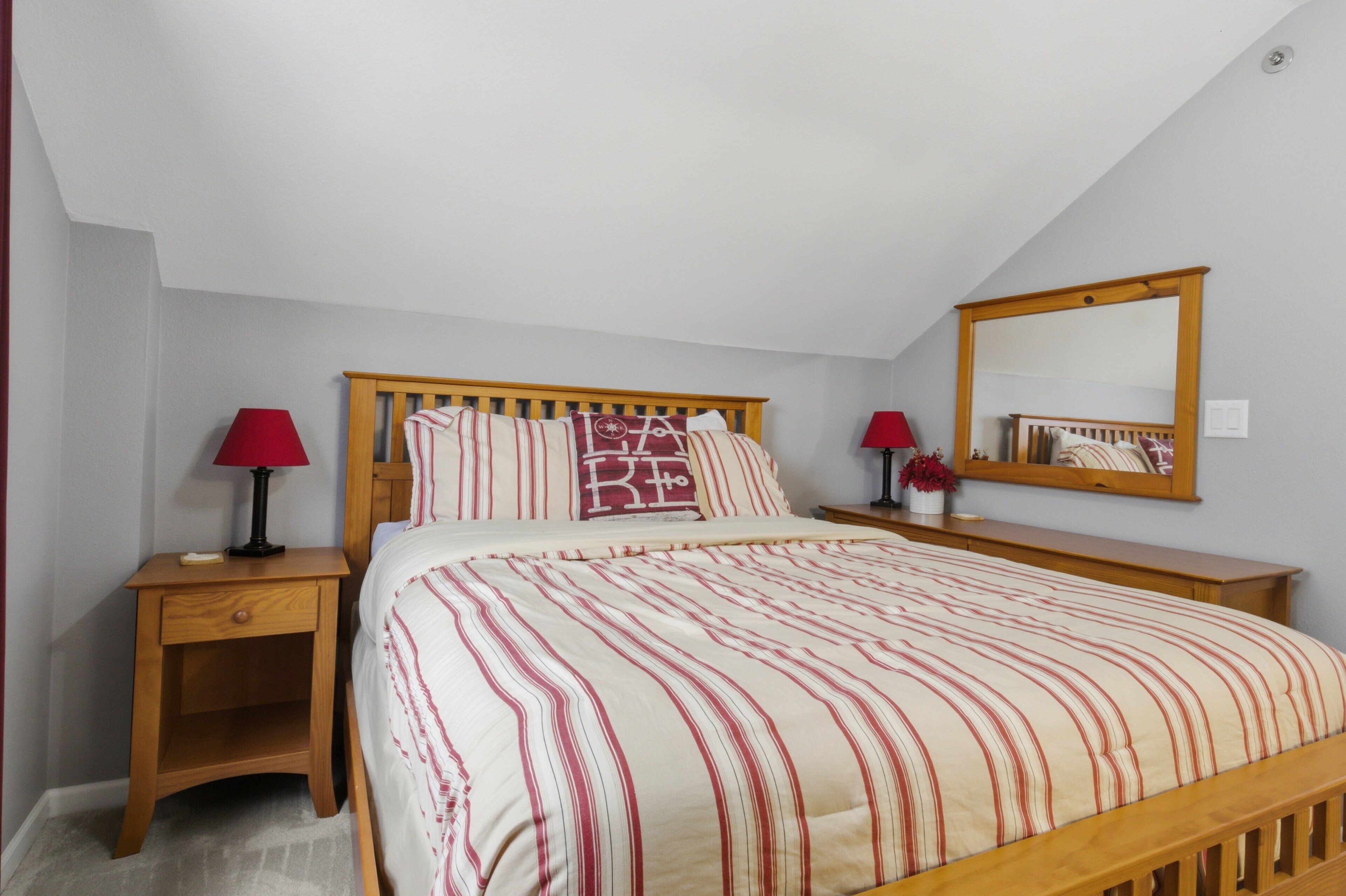 Une chambre à coucher avec un lit en bois, deux tables de chevet, une lampe rouge sur chacune, un miroir et un vase rouge avec une fleur.