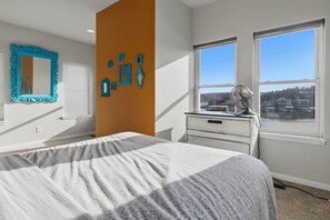 Quarto com cama, penteadeira, espelho e janela com vista para casas.
