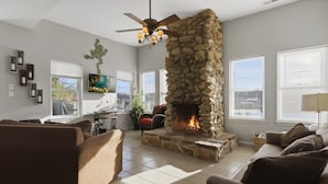 Una sala de estar con chimenea de piedra, ventilador de techo y televisor.