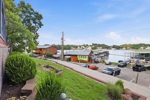 A view of a waterfront property with a parking area, a building with a green facade, and a body of water in the background. - Charming Lakefront House Near Shorty Pants at 21mm (Osage Beach)
