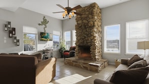 Una sala de estar con chimenea de piedra, ventilador de techo y un ventanal grande.