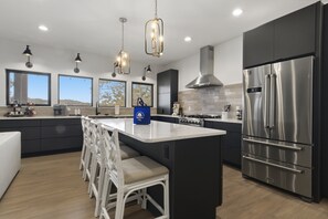 Une cuisine moderne dotée d’un grand îlot central, d’appareils électroménagers en acier inoxydable et de luminaires suspendus.