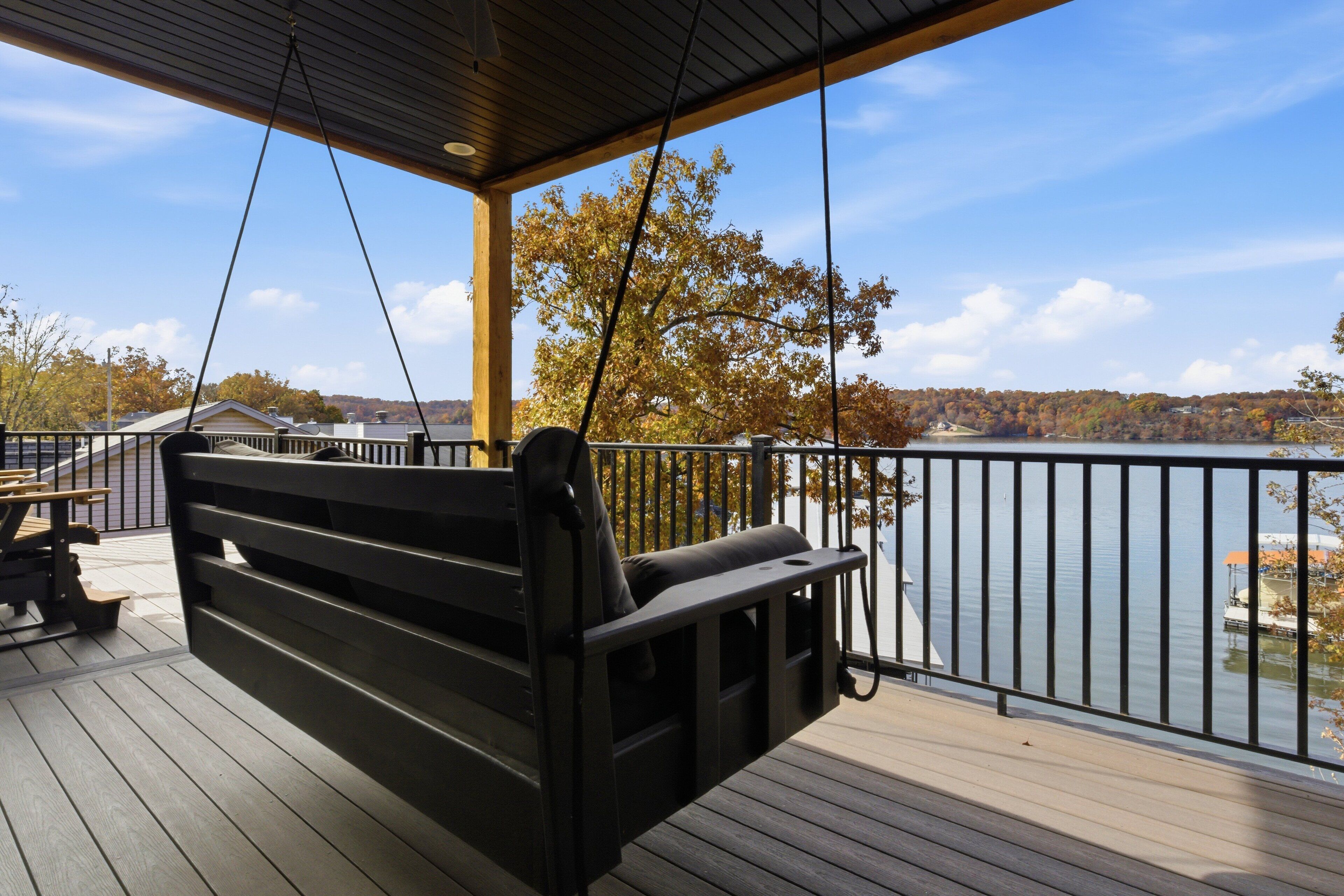 A wooden deck with a swing chair overlooking a lake.