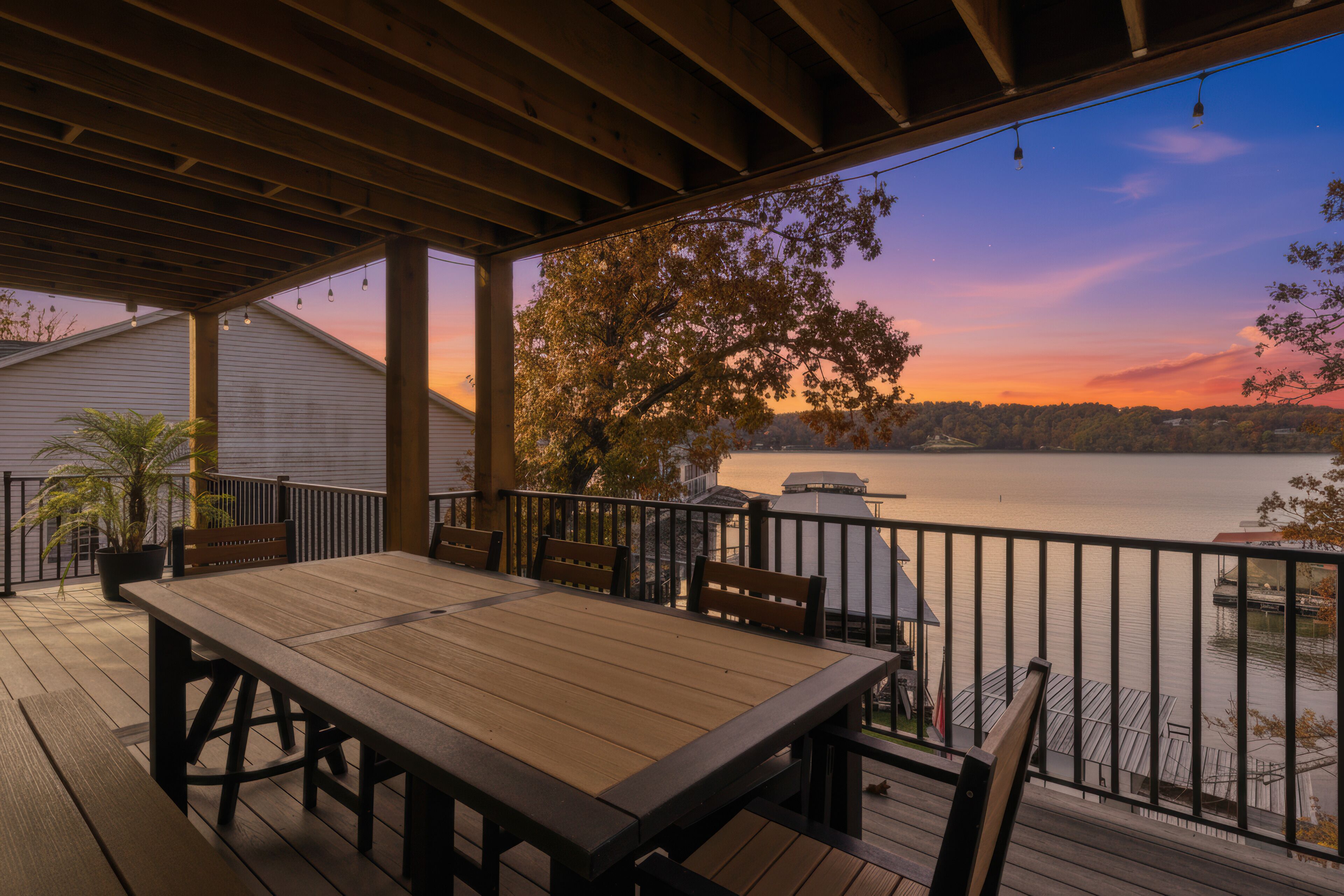 Eine Holzterrasse mit Tisch und Stühlen, mit Blick auf einen See bei Sonnenuntergang.