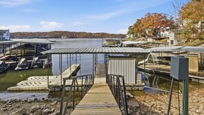 A dock with boats, a covered area, and a building with a metal roof. - New Lakefront Home With Private Dock, Game Room & Firepit at 9MM (Lake Ozark)