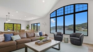 A spacious living room with a large window offering a scenic view of hills and water. - Modern Lakefront Escape The Twelve (Camdenton)