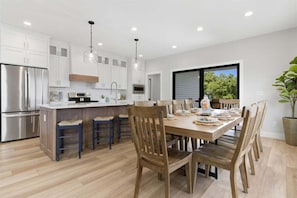 A modern kitchen with white cabinets, stainless steel appliances, and a wooden dining table with chairs. - Modern Lakefront Escape The Twelve (Camdenton)