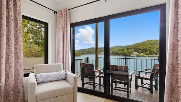 A balcony with a view of a lake and hills, a sofa, and a table with chairs. - Modern Lakefront Escape The Twelve (Camdenton)