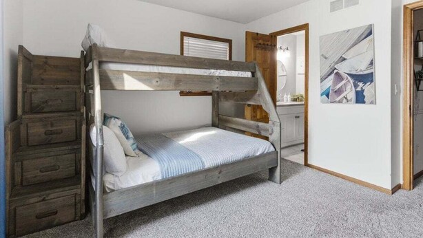 Ein Stockbett mit Holzleiter, eine kleine Kommode und ein Deckenventilator.