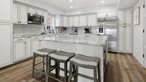 Una cocina moderna con armarios blancos, una isla grande con taburetes de bar, electrodomésticos de acero inoxidable y un rebozado de azulejos.
