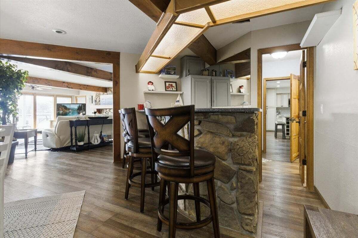 A spacious living area with a stone fireplace, wooden beams, and a view of the outdoors.